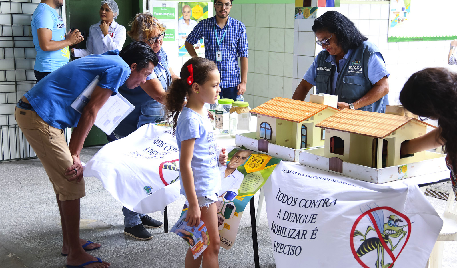 pessoas ao redor de uma mesa com material explicativo sobre arboviroses